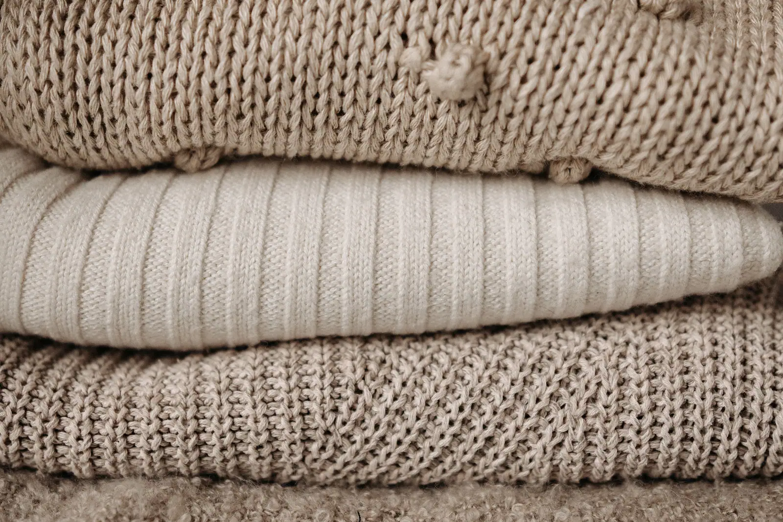 Three folded knits in oatmeal, cream and taupe stacked on top of each other.