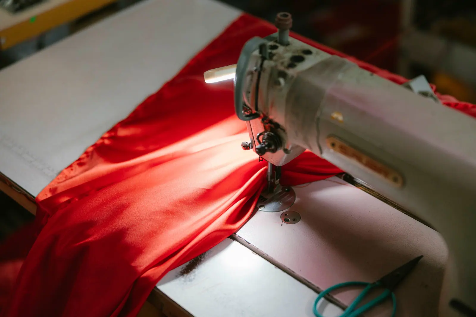 An industrial sewing machine stitching bright red fabric under a work light.