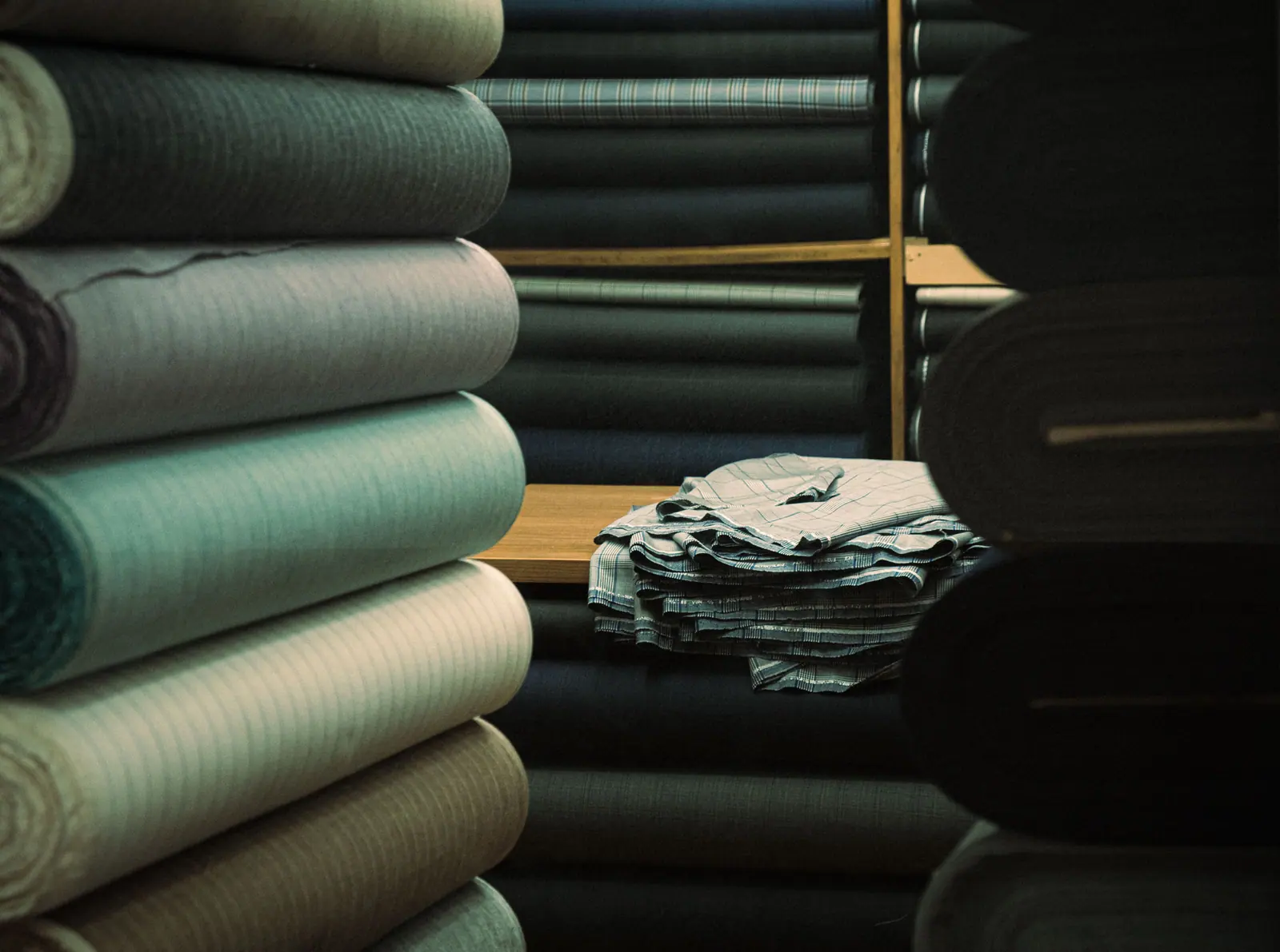 Bolts of green and charcoal fabric stacked on warehouse shelving in low light.